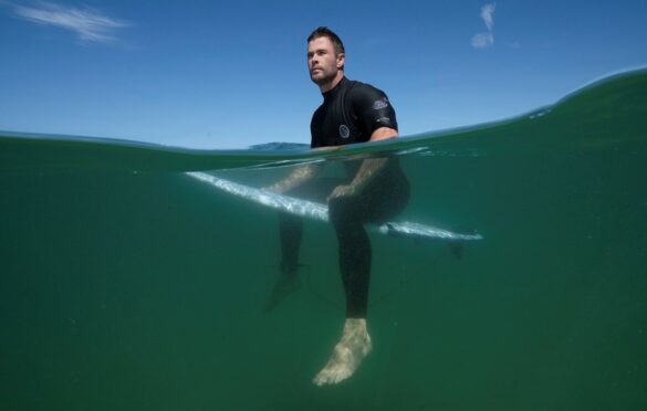 Chris Hemsworth sedí na surfu ve vodě 